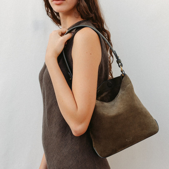 Model wearing STOW London's Midi Curve in Dark Green suede leather featuring the detachable shoulder strap with gold hardware