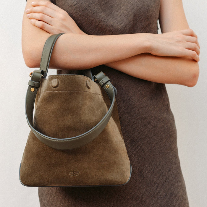 Model wearing STOW London's Midi Curve in Dark Green suede leather featuring the detachable shoulder strap with gold hardware