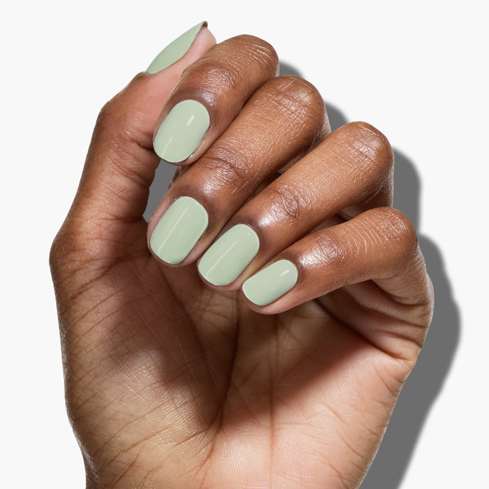 A hand with short, neatly manicured nails painted in LONDONTOWN's Lichen, a calming pale green shade akin to white sage.