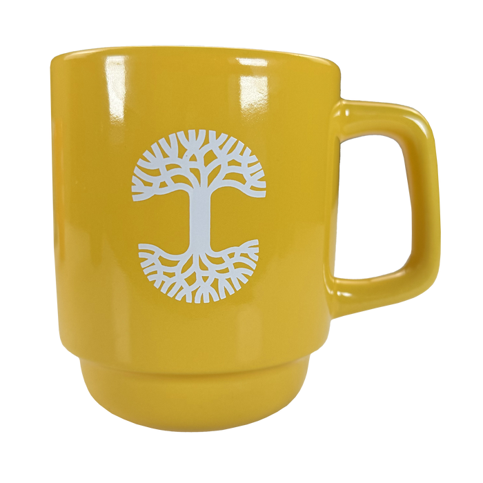 The Logo Stack Mug by Oaklandish is a yellow ceramic mug with a white stylized tree logo in the center, featuring circular branches and roots, a broad handle, and a glossy finish. Displayed on a plain white background.