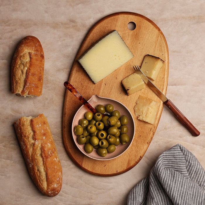 Wooden charcuterie board with cheese, bread and olives on a light background.