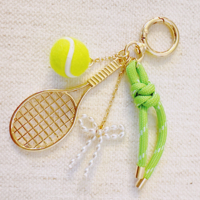 Ellison+Young Match Point tennis bag charm with gold and neon accents, featuring a racket and ribbon details.