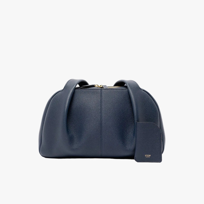 STOW London's Mini Cardholder in Navy pebbled leather with the matching Bowling Bag on a light grey background featuring a small gold embossed logo on the front bottom