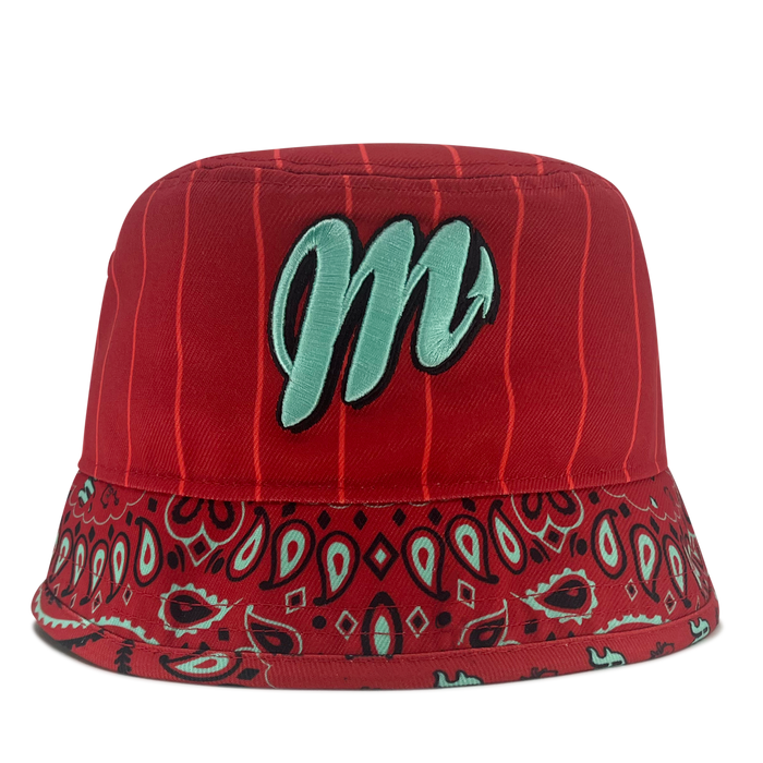 The New Era Diablos Paisley Bucket by Other is a red polyester bucket hat featuring vertical pinstripes, a wide brim with a red, black, and teal paisley bandana pattern, and a large light teal “m” embroidered on the front. The background is plain white.