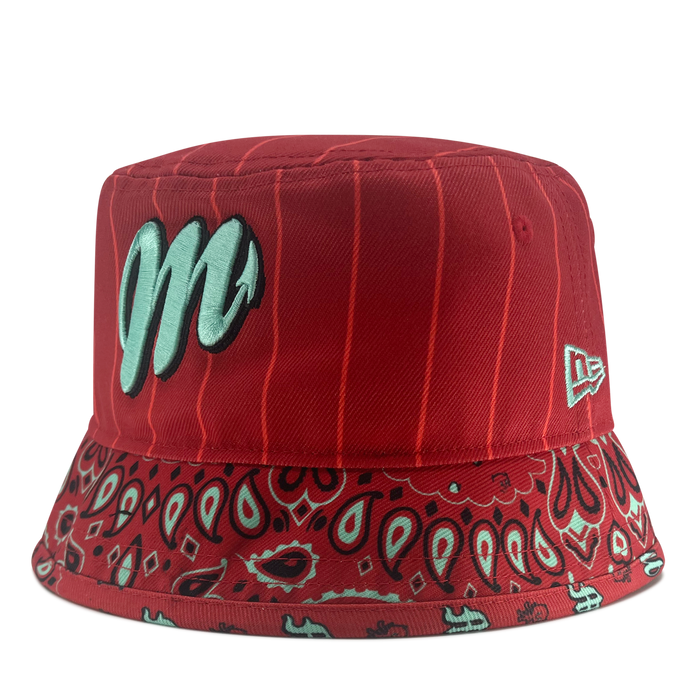 Introducing the New Era Diablos Paisley Bucket by Other—a vibrant red bucket hat made from durable polyester. It features a prominent light blue “M” logo on the front, a white New Era logo on the side, and a patterned brim detailed with red, black, and light blue bandana-inspired paisley designs. Vertical pinstripes complete the look for a stylish finish.