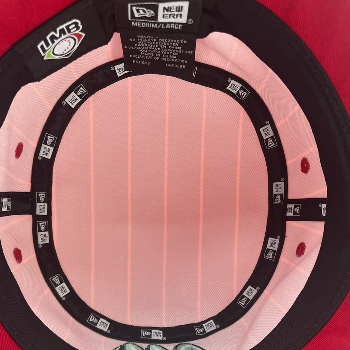 The interior of the New Era Diablos Paisley Bucket hat by Other is displayed, highlighting the black sweatband adorned with New Era logos, the LMB patch, and a size tag labeled “Medium/Large.” Made from soft polyester fabric in a light pink shade, this bucket hat showcases visible stitching and panel lines.