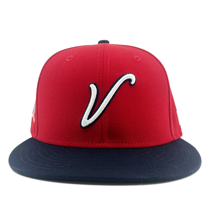 The New Era El Aguila Alt 59FIFTY Cap by Other features a vibrant red crown with a navy blue flat brim. A white, stylized “V” logo adorns the front panel, while the official LMB logo is embroidered on the side. Presented in a pristine, unworn condition against a plain white background, this fitted cap is shown from a centered, front-facing angle.
