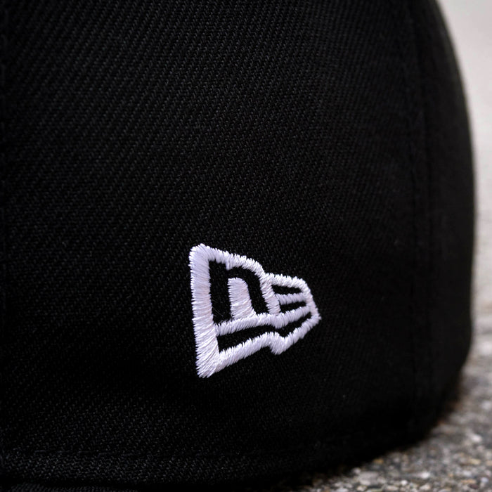 Close-up of the New Era Oakland Roots SC 59FIFTY Fitted Cap in black, showcasing an embroidered white logo. The logo features a stylized "N" followed by a smaller "E" in a continuous line, creating a distinctive design. The texture of the fabric and the precision of the stitching are clearly visible, making it perfect for Oakland Roots SC fans.