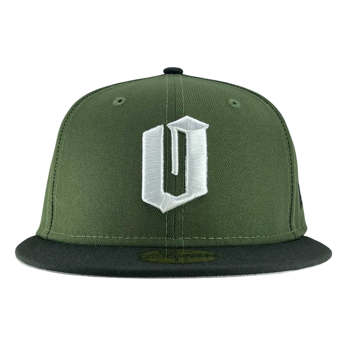 A New Era Official 59FIFTY Fitted Cap by Other, this green snapback features a bold, white embroidered “U” in a stylized font on the front panel and a black flat brim. Inspired by classic fitted cap design, it adds an Oaklandish edge to your style. The plain white background emphasizes the cap’s color and distinctive details.