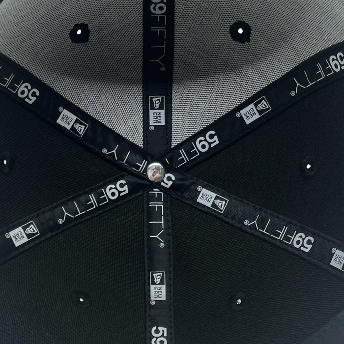 Close-up of the inside of a black New Era Pericos ALT 59FIFTY Cap by Other, featuring stitched labels, gray and black fabric panels, ventilation holes, a central metal button, and “59FIFTY” logos along the black seams. This fitted cap showcases meticulous craftsmanship and iconic branding details.