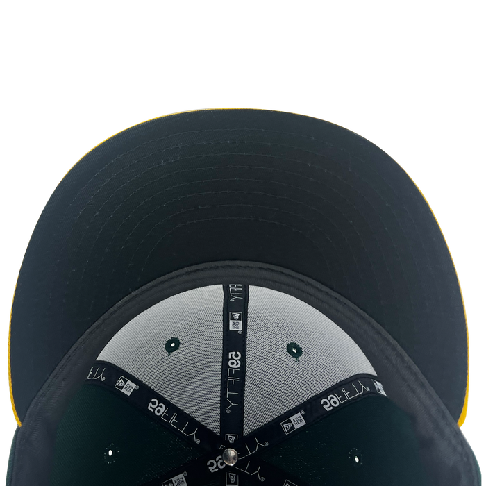 Close-up view of the underside of the New Era Pericos Home 59FIFTY Cap by Other, featuring black, grey, and green panels, a black brim, taped seams with “59FIFTY” and New Era logos, and a small metal button at the center. A subtle yellow edge is barely visible, while the distinctive LMB logo provides an authentic finishing touch.