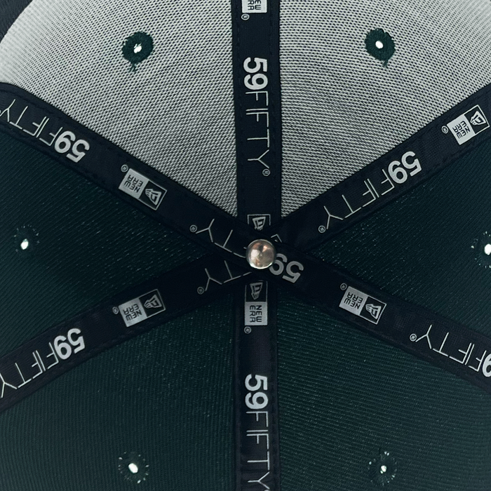 Close-up of the inside crown of a green New Era Pericos Home 59FIFTY Cap by Other, featuring stitched black and white branded taping, white mesh panels with green embroidered eyelets, and a metal button at the center intersection. This detailed view showcases the quality craftsmanship behind the Pericos Home 59FIFTY Cap, making it a standout addition to any collection.