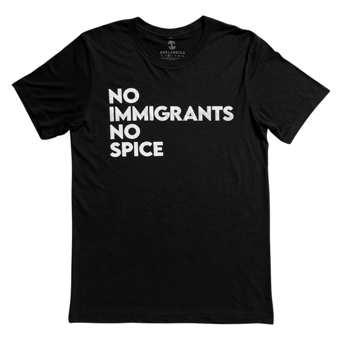 The NINS Classic Tee by Oaklandish features a round neck and short sleeves, with bold white text that reads "NO IMMIGRANTS NO SPICE" arranged in three lines against its black fabric. Faintly branded inside the collar, this shirt proudly supports immigrant rights and is presented laid flat against a plain white background.