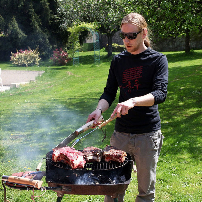 Person using giant Opinel knife and fork to barbecue meat on outdoor grill.