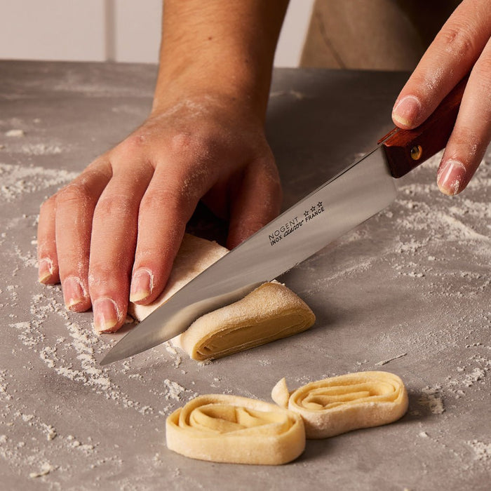 Hands holding knife and cutting raw pasta.