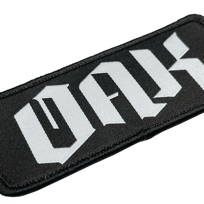 A close-up of the OAK Official Patch by Oaklandish, featuring a rectangular black embroidered design with the words "OAK with the drip" in large, stylized white letters. The letters boast a gothic, angular design and the patch's edges are neatly sewn with black thread. The background is plain white.
