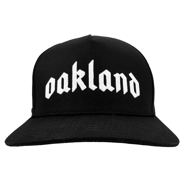 The Oaklandish "Oakland 68s Panel Cap" is a black snapback hat with "oakland" boldly embroidered in white gothic letters on the front, shown from the front against a plain white background.