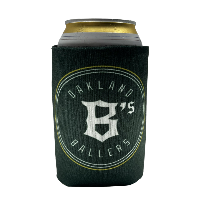 A can of beverage is held in a dark green Oakland Ballers 12oz Can Cooler, showcasing the logo of the new professional baseball team, the "Oakland Ballers." The logo consists of a stylized "B" and the text "OAKLAND BALLERS" encircling it, all in white letters. The beverage can has a silver top with a partially visible gold tab.