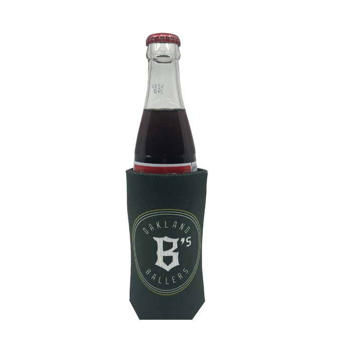 A beverage bottle with a dark-colored drink is placed inside the Oakland Ballers 16oz Can Cooler, which is green and features the bold logo and text: "OAKLAND 95 BALLERS," representing the professional baseball team from the Pioneer League, with a prominent 'B' and '95' at its center. The beverage looks dark red or brown.
