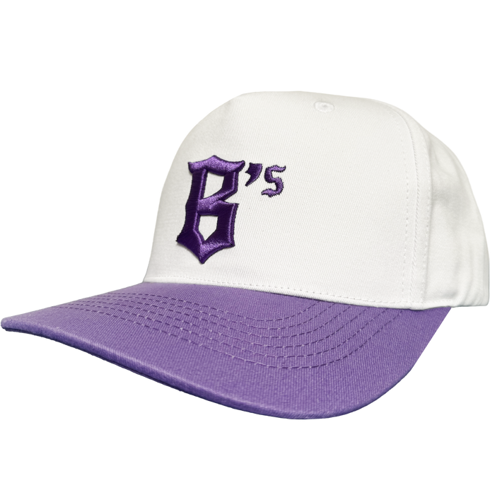 The Oakland Ballers 5 Panel Cap by Oakland Ballers is a white snapback featuring a purple brim and a raised, purple embroidered “B’s” in gothic font on the front, referencing the Oakland Ballers baseball team. The cap is photographed against a plain white background.
