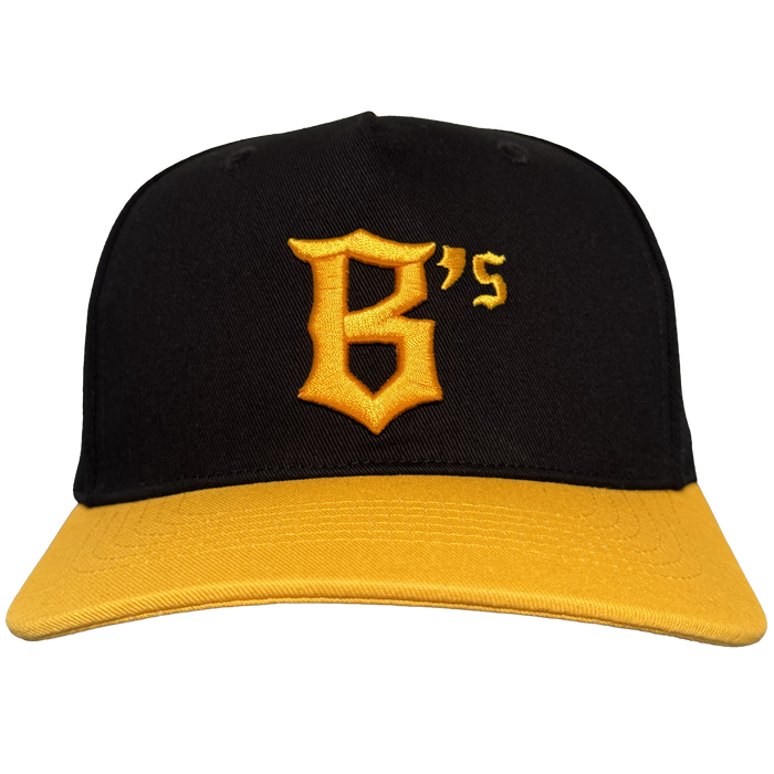 The Oakland Ballers 5 Panel Cap by Oakland Ballers is a black snapback with a yellow brim, featuring a bold yellow “B” and small “’S” on the front, inspired by the Oakland Ballers. The background is plain white.