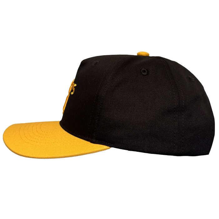 The Oakland Ballers 5 Panel Cap by Oakland Ballers is a black snapback with a yellow brim and button, visible stitching, eyelets, and part of a yellow embroidered letter—ideal for any Oakland Ballers fan. Shown side-on on a white background.
