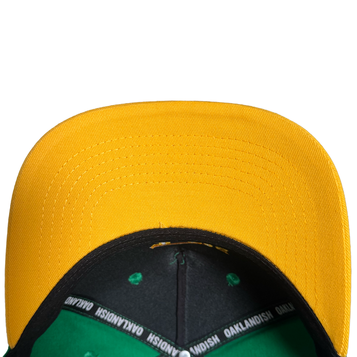 A top-down close-up of the Oakland Ballers 5 Panel Cap by Oakland Ballers, featuring a bright yellow bill, black and green interior with “OAKLANDISH” printed on the lining, all set against a plain white background.