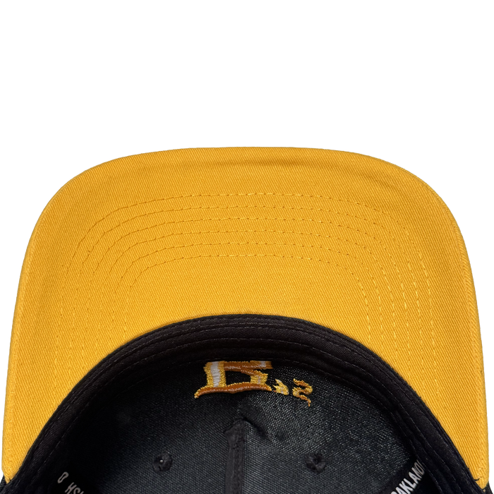 A close-up, top-down view of the Oakland Ballers 5 Panel Cap shows its yellow stitched brim and black underside with a gold embroidered "E" and "32," all set against a plain white background—a tribute to the Oakland Ballers spirit.
