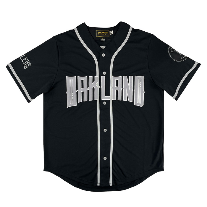 The Oakland Ballers Button Up Jersey by Oakland Ballers features a black design with white buttons, sleeve, and collar trim. "OAKLAND" is boldly printed across the chest, representing the Pioneer League baseball team. White details accent sleeves and cuffs.