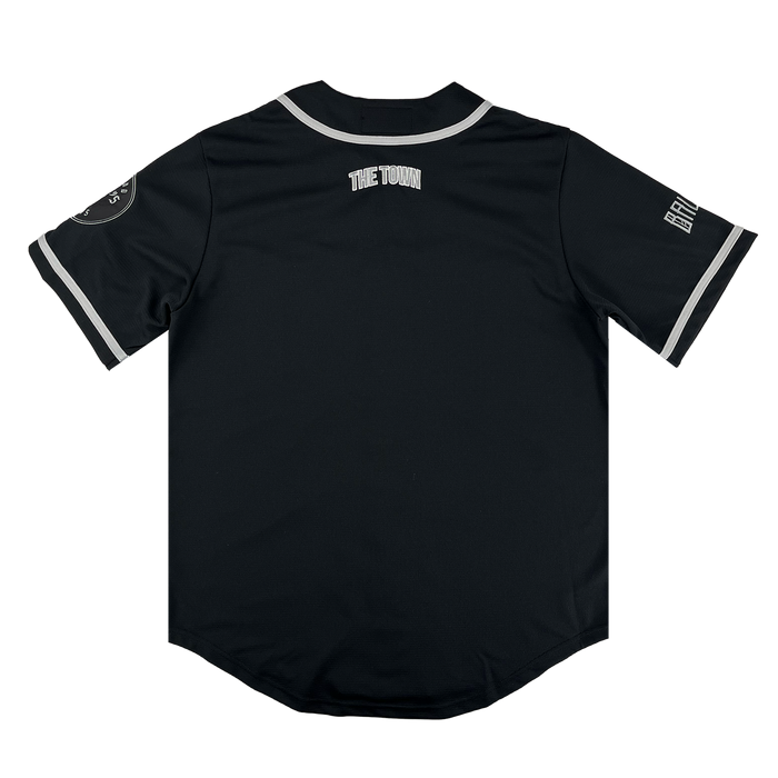 The Oakland Ballers Button Up Jersey by Oakland Ballers features "THE TOWN" on the upper back, white-trimmed sleeves, a patch on the left sleeve, and Oakland Ballers team lettering on the right sleeve. Shown from the back on a white background.