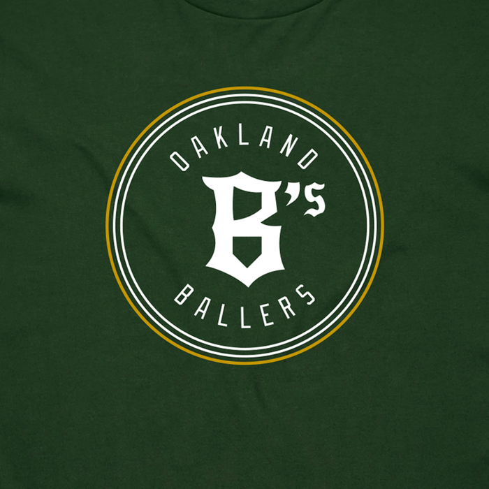 The Oakland Ballers Classic Tee from the Oakland Ballers brand is a dark green T-shirt featuring a white and yellow circular emblem in the center. Inside the circle, the text "OAKLAND BALLERS" appears at both the top and bottom, with a stylized "B's" in the center. The design celebrates Oakland’s new professional baseball team in the Pioneer League, giving it a sporty, team logo aesthetic.