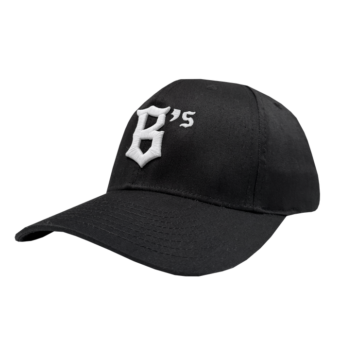 The Oakland Ballers Flexfit Cap is a black polyester-spandex baseball cap with a curved brim and white embroidered “G’s” in Gothic font. The Oakland Ballers brand cap is shown angled on a plain white background, showing the front and side.