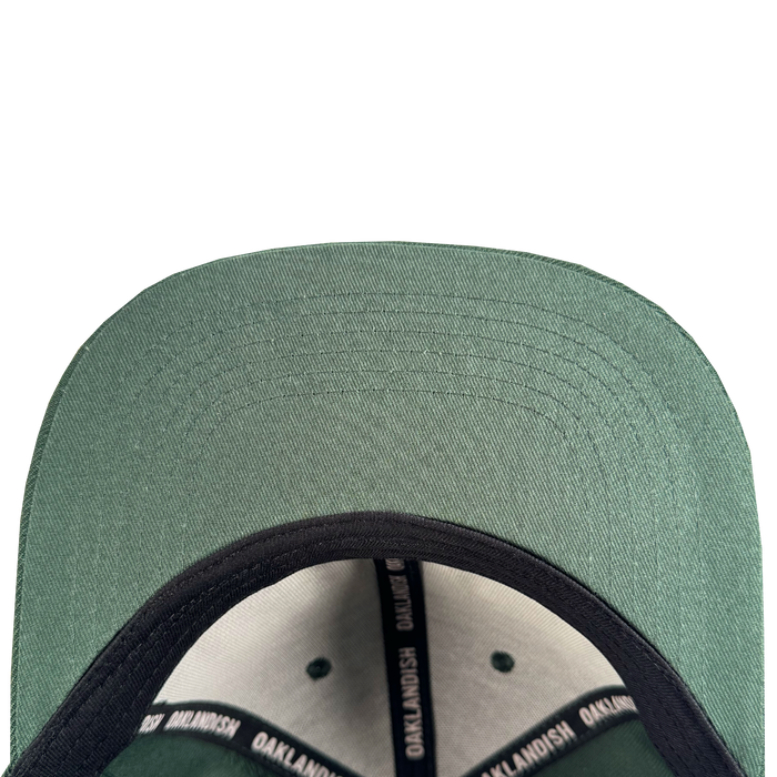 Close-up of the Oakland Ballers Flexfit Cap: a green baseball hat with a black inner lining and sweatband featuring repeated “OAKLANDISH” text, celebrating Oakland Ballers pride. Detailed stitching accents the underside of the brim.
