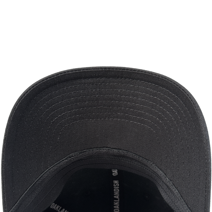 Close-up view of the underside of the Oakland Ballers Flexfit Cap, featuring a curved brim with visible concentric stitching and part of the interior, crafted from durable polyester by Oakland Ballers, with some partially visible printed text.