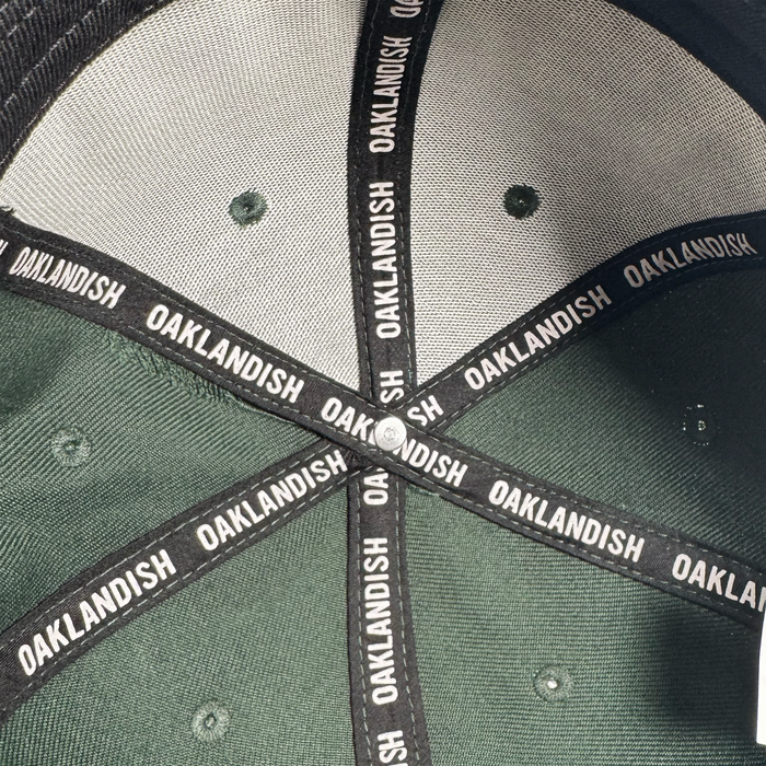 Close-up of the Oakland Ballers Flexfit Cap's inside crown reveals black seam tape with repeating "OAKLANDISH" in white, subtly celebrating the new Oakland Ballers pro baseball team in the Pioneer League.