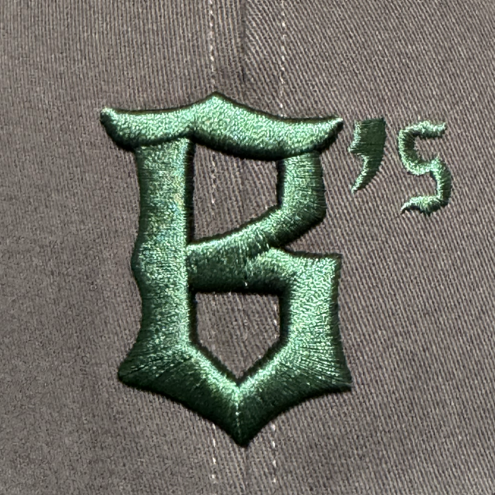 A close-up of the Oakland Ballers Logo Hat by Oakland Ballers shows gray fabric with a large dark green embroidered gothic "B," plus an apostrophe and "S," representing the new Oakland Pioneer League baseball team’s logo.