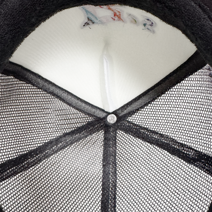Close-up of the Oakland Ballers Pride Trucker by Oakland Ballers, showing intersecting black mesh lines, a central silver button, and white fabric with faint colorful embroidery suggesting a team-inspired design.