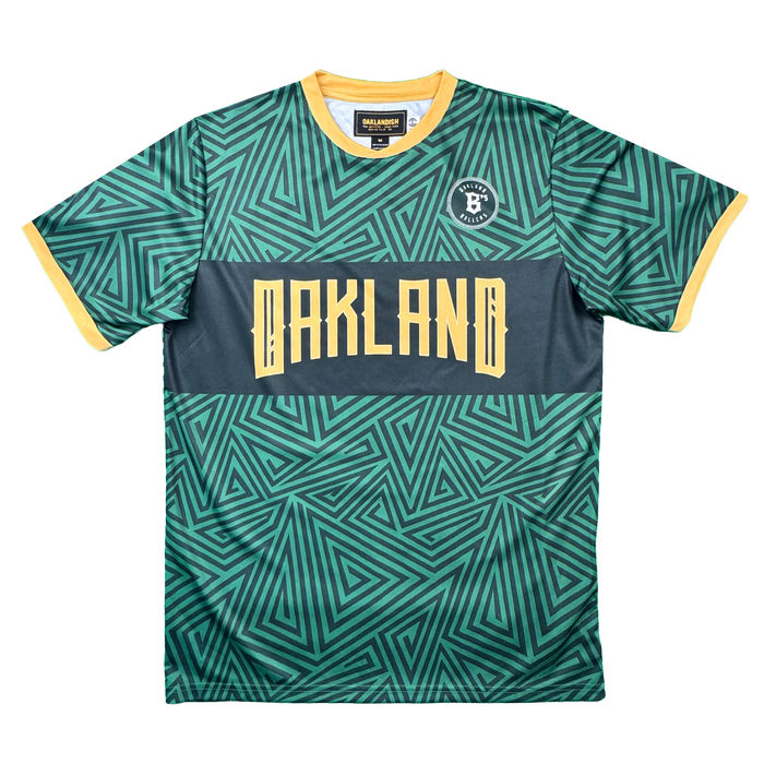 The Oakland Ballers SC Jersey by Oakland Ballers features a vibrant green color with yellow geometric patterns, yellow sleeve cuffs and collar, and a dark gray band across the chest showcasing "OAKLAND" in bold yellow letters. A round logo with a "B" appears on the left chest, making this authentic pro baseball jersey perfect for fans of the Oakland Ballers or anyone seeking gear inspired by the iconic Oakland baseball team.