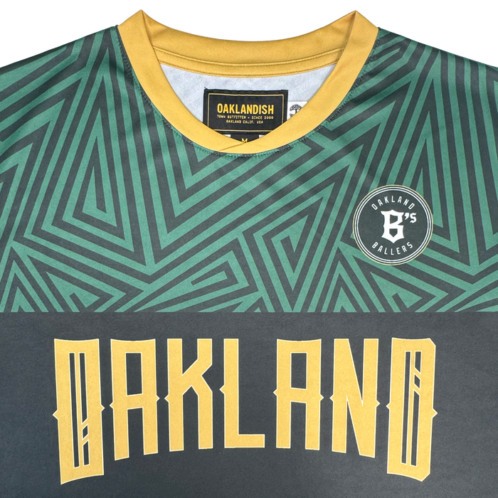 A close-up of the Oakland Ballers SC Jersey, a pro baseball jersey featuring green geometric patterns, a yellow collar, bold yellow "OAKLAND" lettering on the front, and a round patch reading "Oakland B's Ballers." The brand label inside the collar displays "Oakland Ballers," capturing the spirit of the Oakland Ballers baseball team.