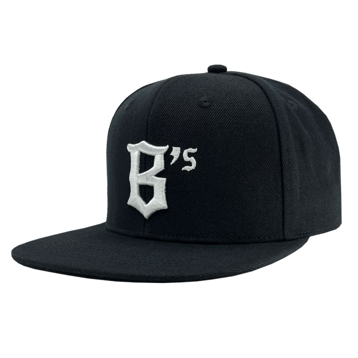 The Oakland Ballers Snapback is a black flat-brim baseball cap featuring an embroidered design on the front panel. The design showcases the character "B" with a small "s" beside it in white thread, styled in an angular, gothic font. Inspired by the spirit of the Oakland Ballers, this cap boasts a classic six-panel structure and a top button.