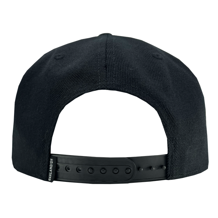 The Oakland Ballers Snapback, viewed from the back, showcases adjustable black plastic snaps for sizing along with a small black fabric tag on the left side near the strap. The slightly textured fabric makes this cap perfect for fans of professional baseball teams like the Oakland Ballers or those in the Pioneer League.