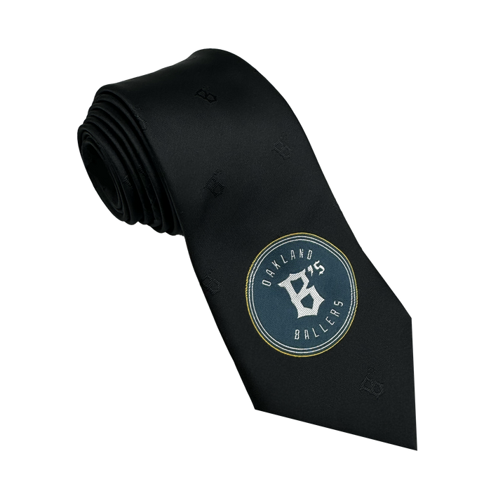 The Oakland Ballers Tie from the Oakland Ballers brand is a rolled black tie that showcases the team's logo near the bottom. The circular design prominently features "Oakland Ballers" with a stylish white "O" and "B," complemented by subtle embossed letters for an elegant touch, celebrating the essence of Pioneer League style.