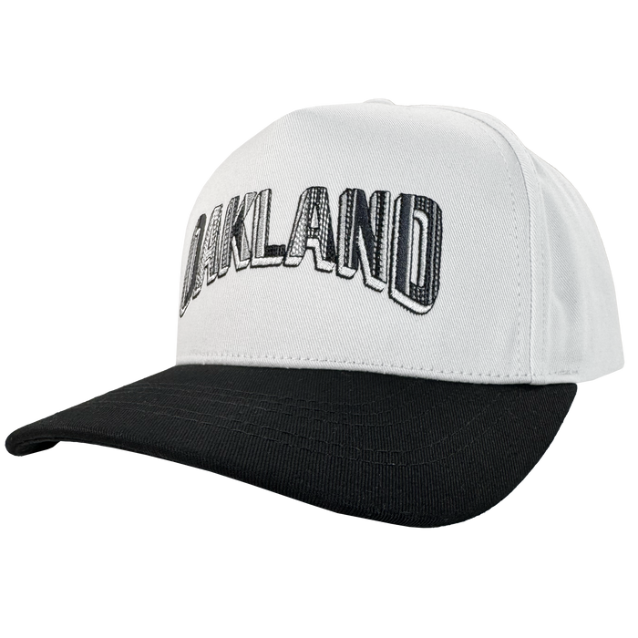 The Oakland Ballers Oakland Beisbol 5 Panel Cap features a white snapback with black brim and bold “OAKLAND” outlined letters—perfect for any baseball fan. The angled view highlights the front and side of this stylish cap.