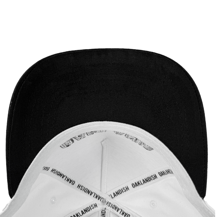The Oakland Beisbol 5 Panel Cap by Oakland Ballers is a white snapback hat with a black underside of the brim. Inside seams have "OAKLANDISH" printed repeatedly on white tape. Shown from above on a plain white background.