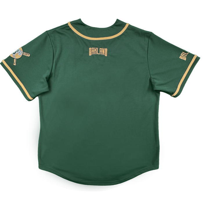 The Oakland Ballers Oakland Button Up Jersey is green with gold trim on the sleeves and collar, "OAKLAND" in gold text on the upper back, a Pioneer League patch on the left sleeve, and "BALLERS" in gold on the right sleeve. Laid flat, back facing up.