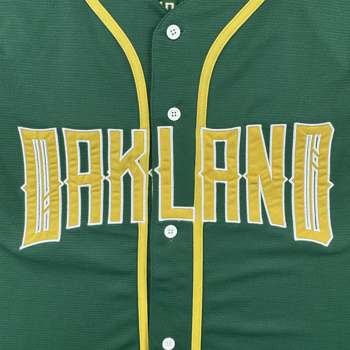 The Oakland Ballers’ Oakland Button Up Jersey is green with gold and white trim, features "OAKLAND" in bold gold outlined in white, and has four white buttons down the center.