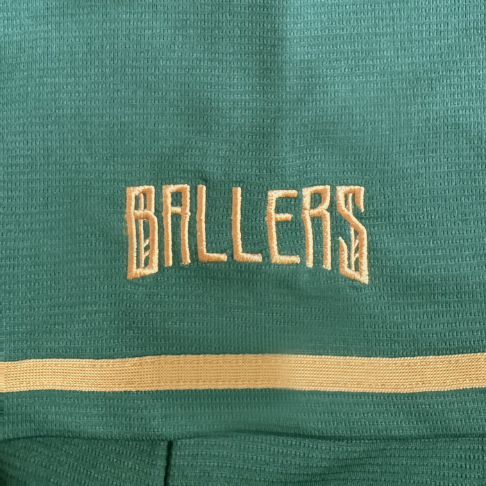 A close-up of green textured fabric from the Oakland Ballers’ Oakland Button Up Jersey, featuring “BALLERS” embroidered in beige block letters and a beige stripe below.
