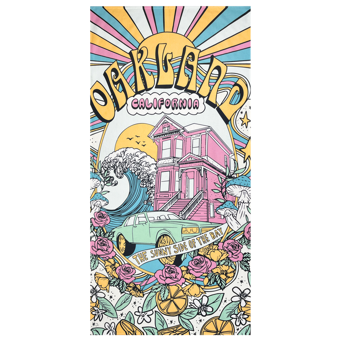 The Oakland Dream Towel by Oaklandish features a vibrant illustration of "Oakland California" with a sunburst background. At its center, a wave and a pink Victorian-style house stand out, surrounded by multi-colored flowers, oranges, and a green car adorned with the words "The Sunny Side of the Bay.
