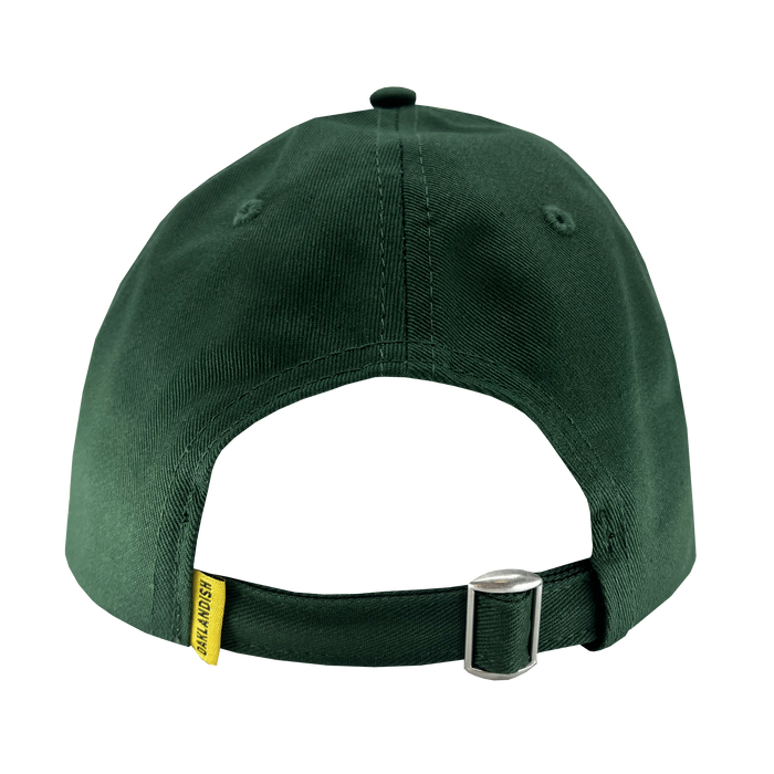 The image shows the back view of the Oakland Flag Dad Hat by Oaklandish in dark green. It features a yellow fabric tag on the left side with "OAKLANDISH" in black text, and includes a metal buckle for size adjustment. The smooth, slightly shiny fabric evokes the vibrant hues of the Oakland flag.