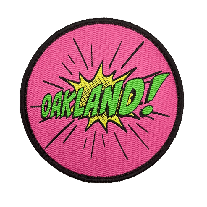 Embroidered iron-on patch with Oakland wordmark in comic cartoon punch style in pink, green and yellow.